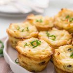 Gourmet muffin tin potato cups garnished with fresh chives, arranged on a white plate.