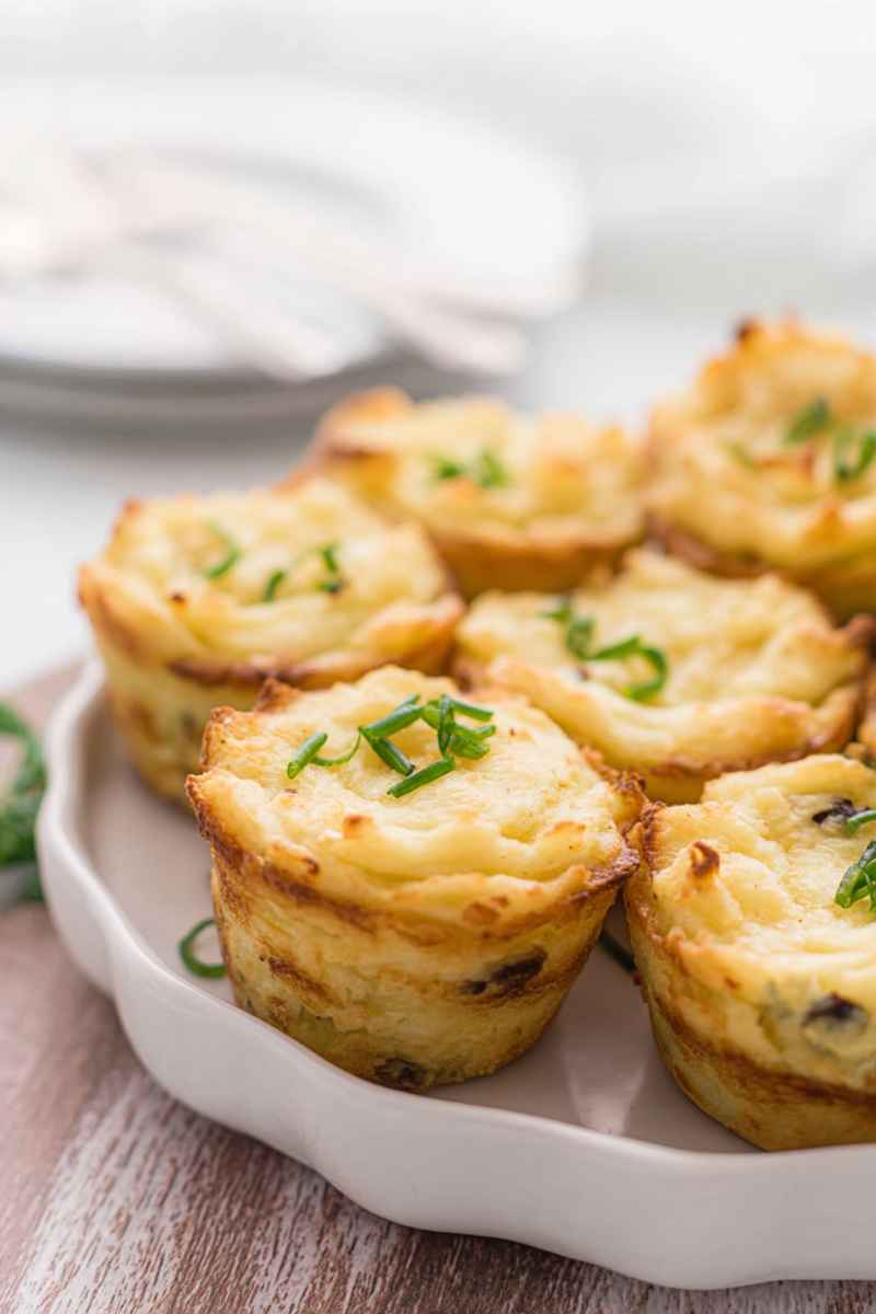 Gourmet muffin tin potato cups garnished with fresh chives, arranged on a white plate.