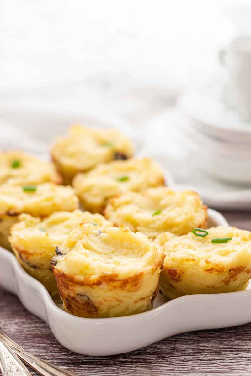 Golden-brown muffin tin potato cups garnished with fresh green onions, served on a white baking dish.