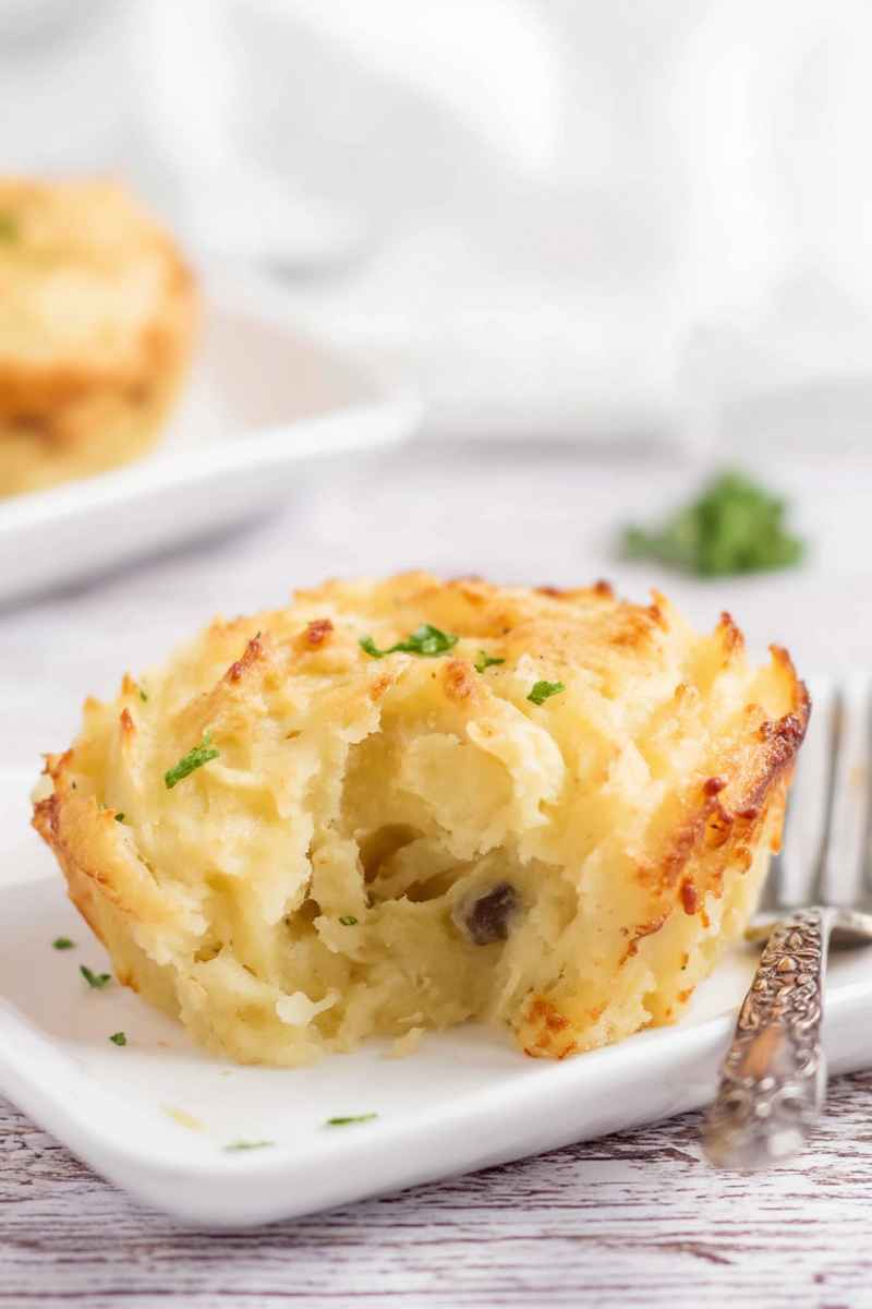 A close-up of a baked potato cup with a golden crust, garnished with fresh herbs, served on a white plate.