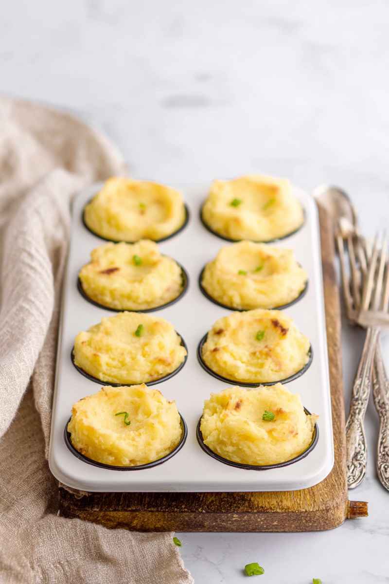 Baked potato cups in a white muffin tin, golden brown and garnished with green onions.