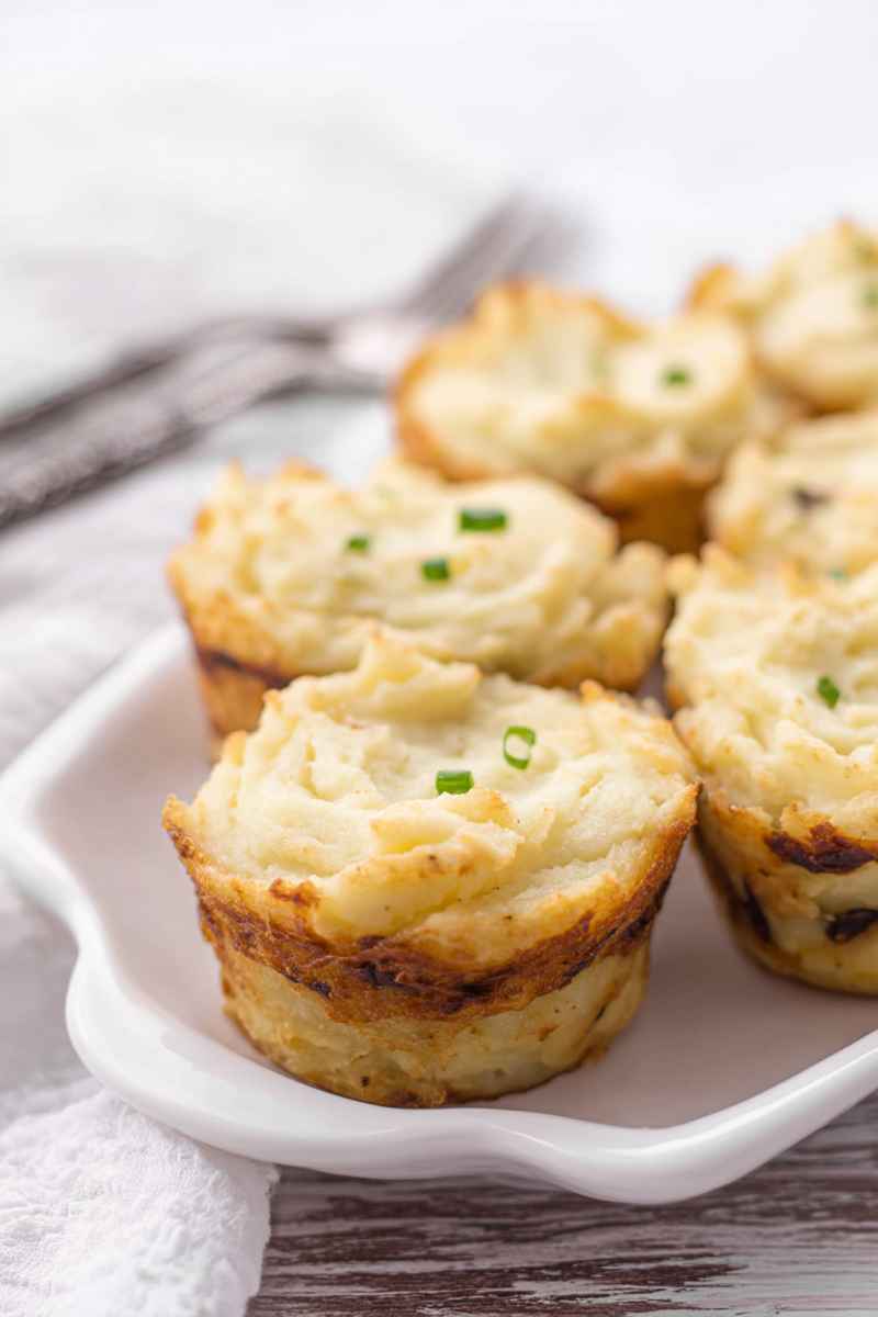 Fluffy muffin tin potatoes with golden edges, garnished with green onions, served on a white plate.
