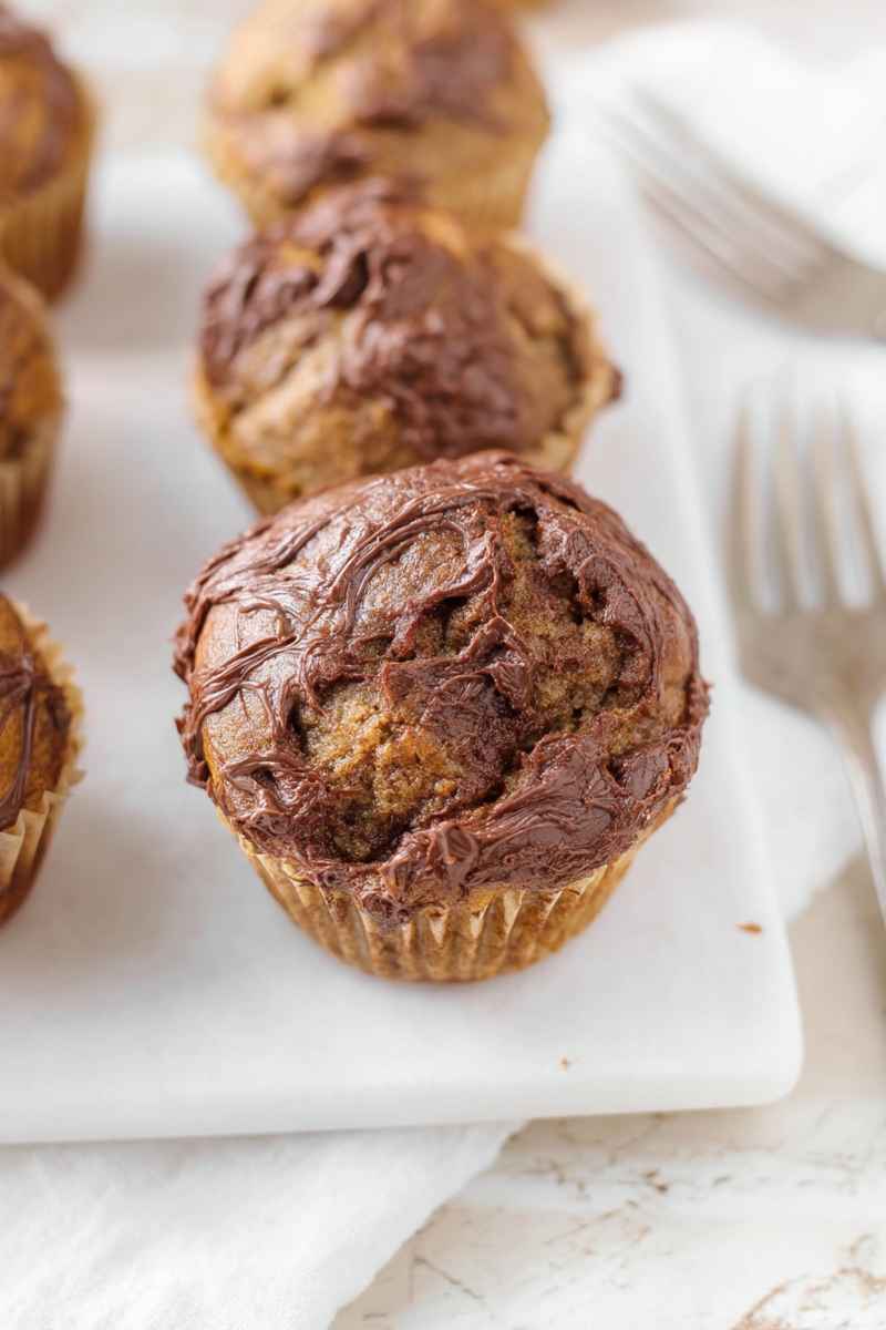 Golden banana muffins with a glossy Nutella swirl, placed on a white plate.