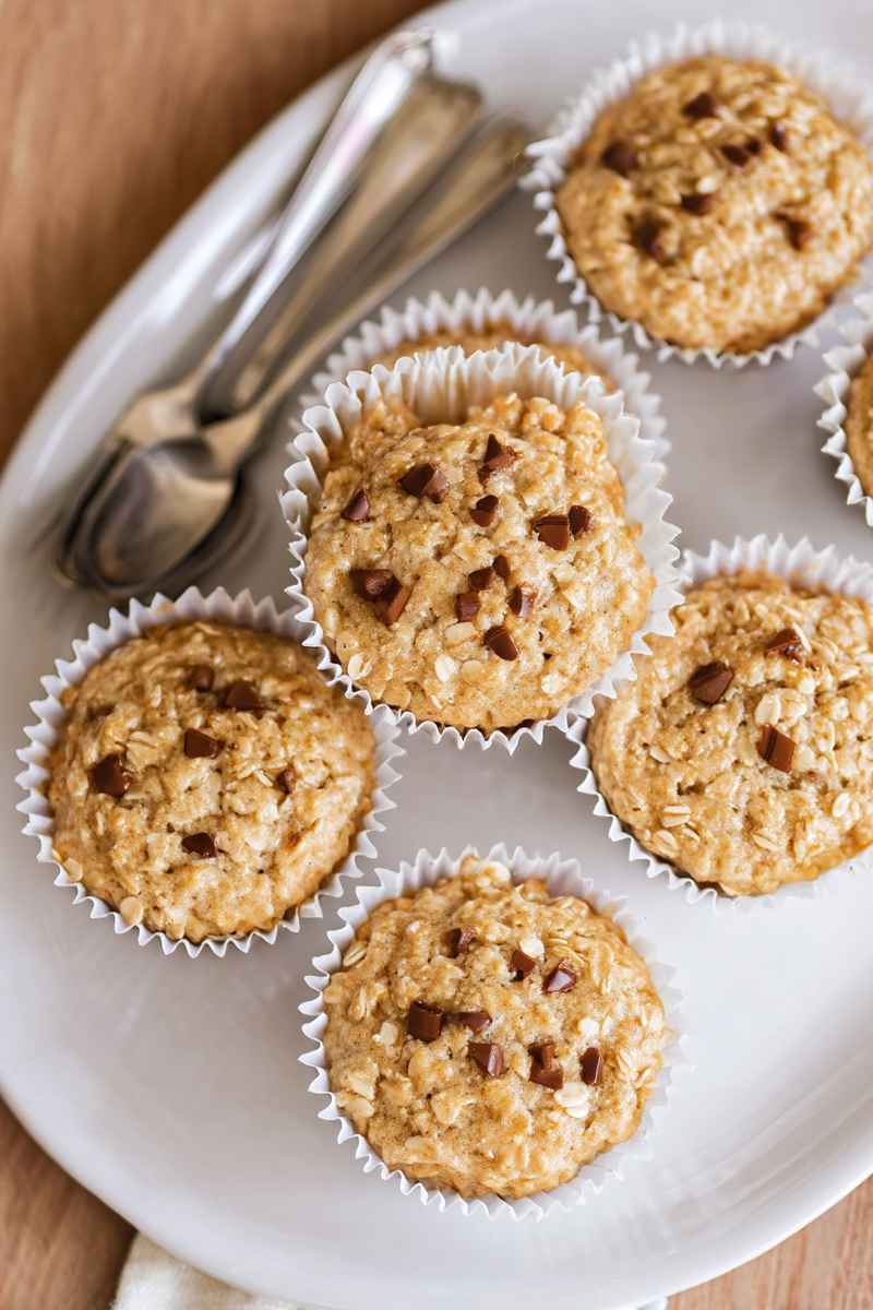 A close-up of oatmeal muffins with chocolate chips, arranged on a white plate with spoons nearby.