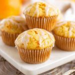 Close-up of orange muffins with white icing, displayed on a marble surface.