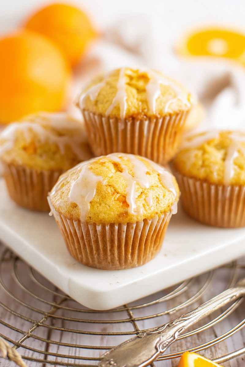 Close-up of orange muffins with white icing, displayed on a marble surface.