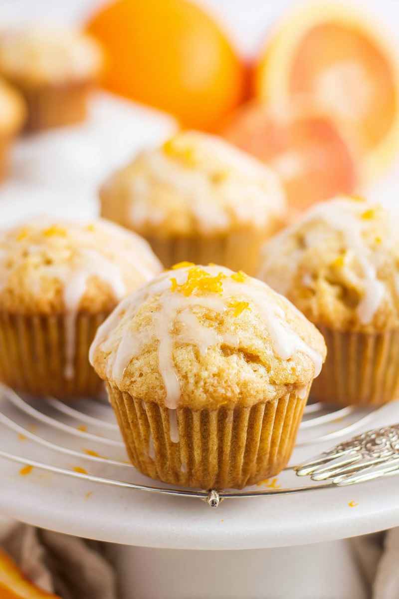 Orange muffins with white glaze and orange zest, presented on a plate.