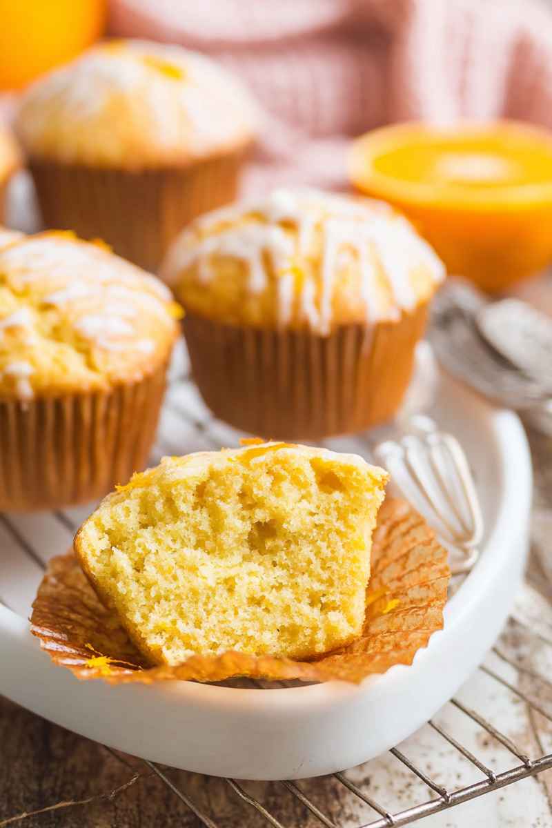 Cross-section of a golden-orange muffin showing its moist interior, surrounded by whole muffins.