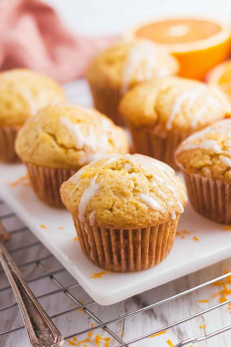 A batch of freshly baked orange muffins with white glaze, arranged on a marble tray.