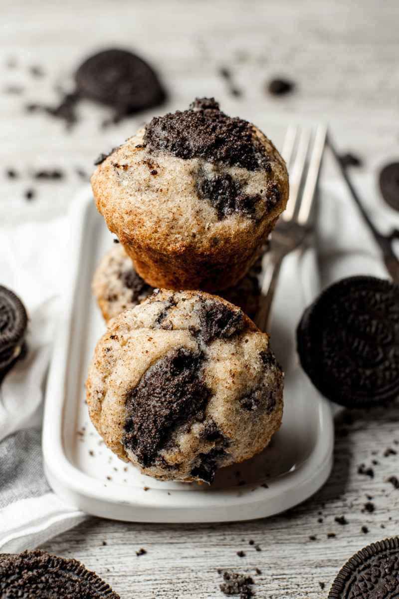 Oreo muffins stacked on a white plate, surrounded by whole Oreos and crumbs, ready to be enjoyed.
