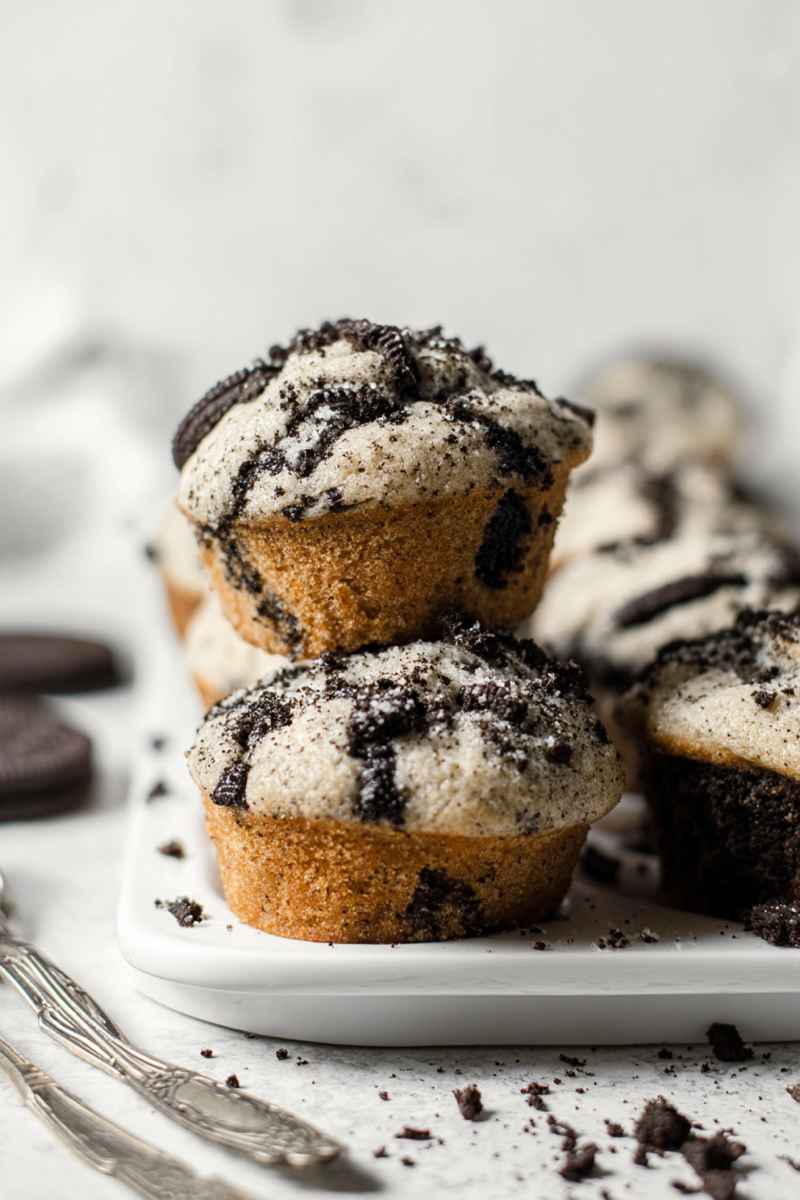 Stacked Oreo muffins on a white plate, highlighting their golden-brown crust and Oreo-speckled interior.