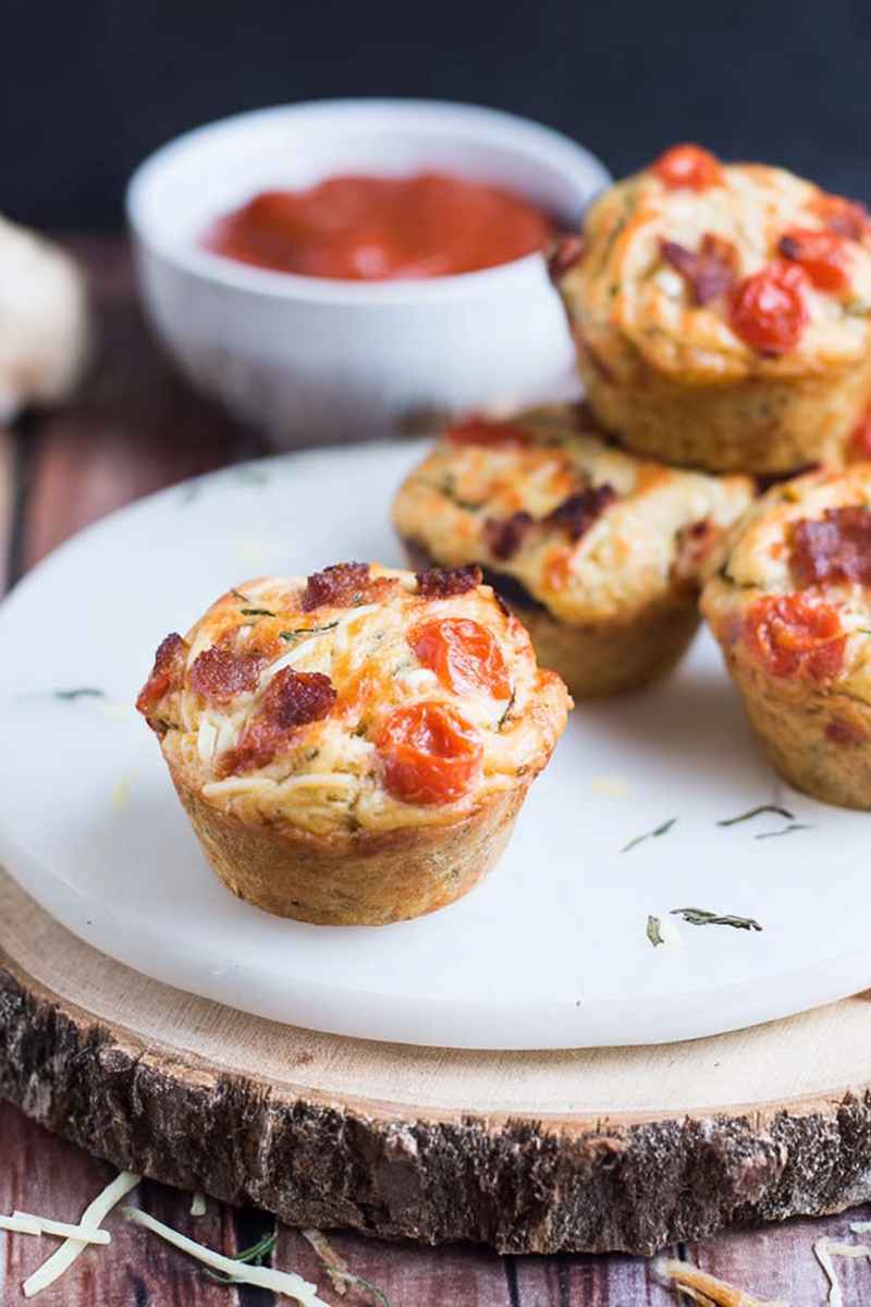 A plate of pizza muffins garnished with fresh herbs, surrounded by marinara sauce and additional toppings.
