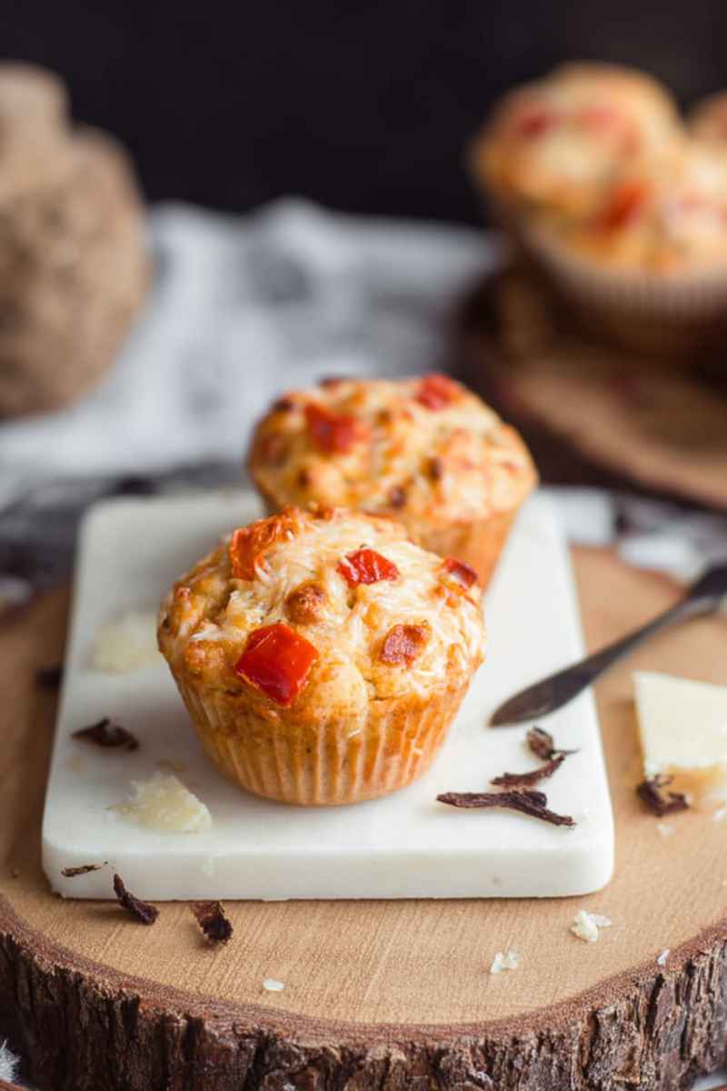 Delicious pizza muffins with melted cheese and colorful toppings served on a marble board.