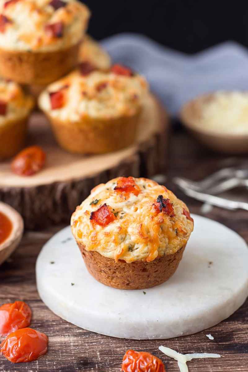 Baked pizza muffins topped with melted cheese and diced tomatoes, presented on a wooden surface.