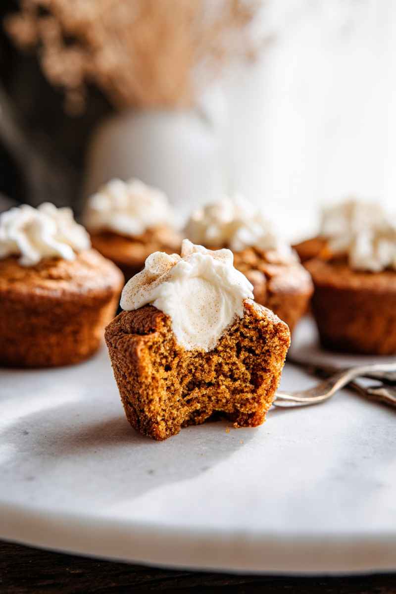 A close-up of a partially eaten pumpkin muffin with frosting, showcasing its moist texture.