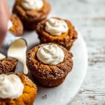 Pumpkin muffins topped with frosting, being drizzled with additional cream from a spoon.