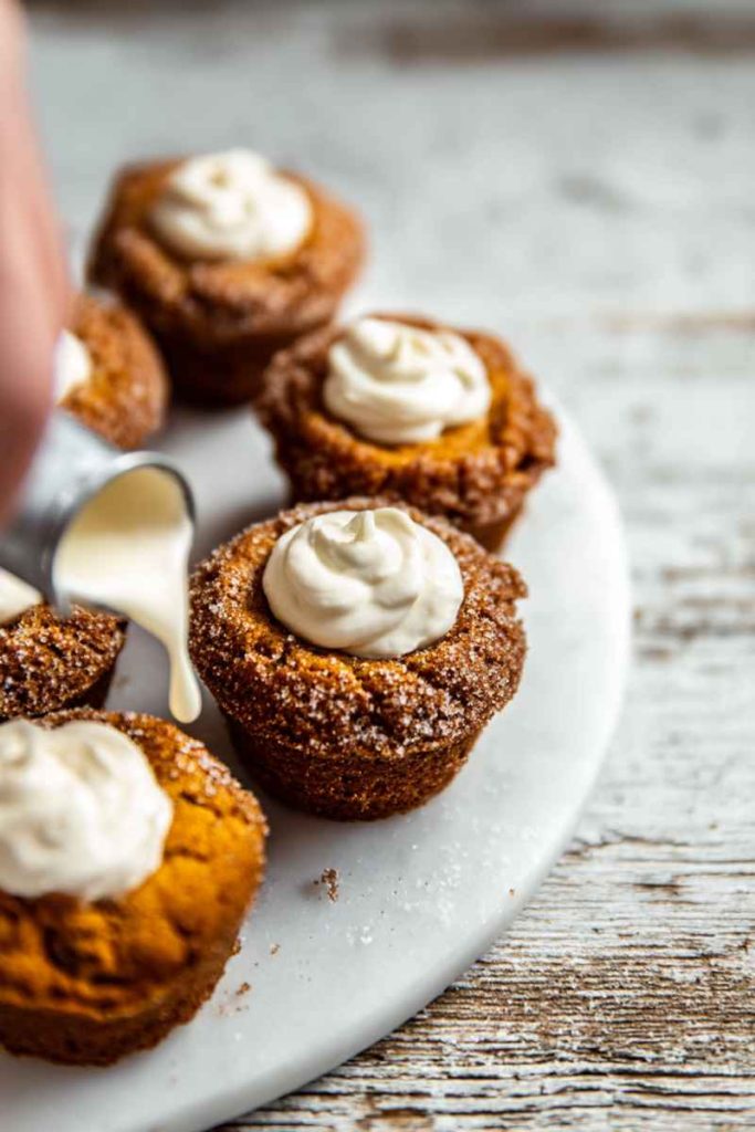 Pumpkin muffins topped with frosting, being drizzled with additional cream from a spoon.
