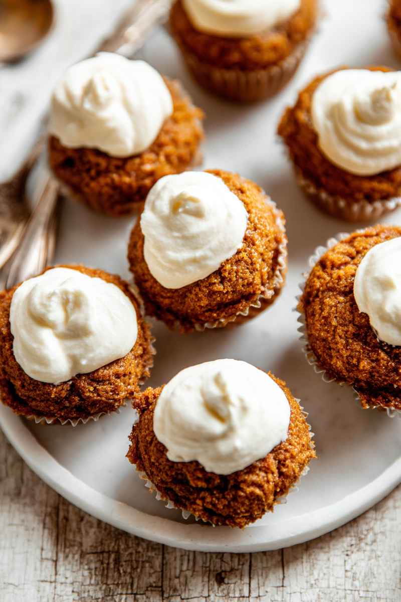 Pumpkin muffins topped with fluffy white frosting, arranged on a white plate.