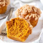 A sliced pumpkin muffin revealing its moist interior, topped with a cinnamon streusel and vanilla glaze.