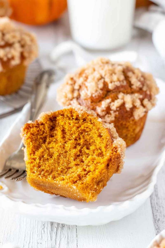 A sliced pumpkin muffin revealing its moist interior, topped with a cinnamon streusel and vanilla glaze.