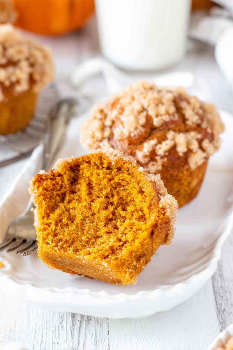 A sliced pumpkin muffin revealing its moist interior, topped with a cinnamon streusel and vanilla glaze.