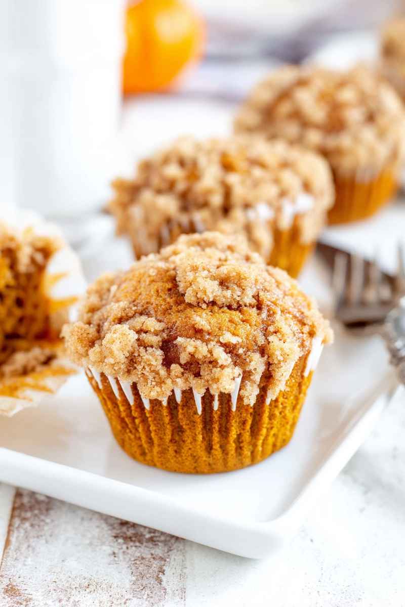 Golden-brown pumpkin muffins topped with a crunchy cinnamon streusel and drizzled with vanilla glaze, sitting on a white plate.