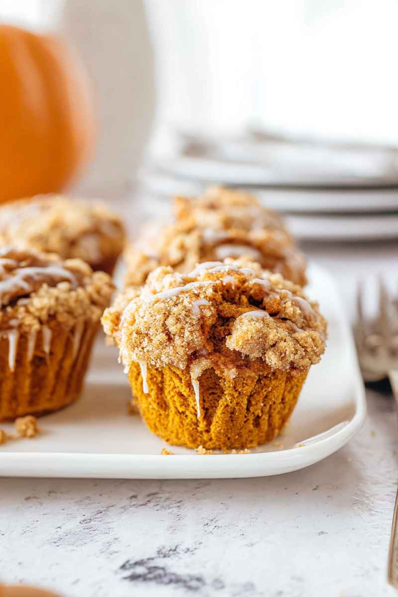 Pumpkin muffins with a generous streusel topping and vanilla glaze, displayed on a white plate.