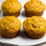 Four golden pumpkin zucchini muffins arranged neatly on a white plate, emphasizing their homemade appeal.