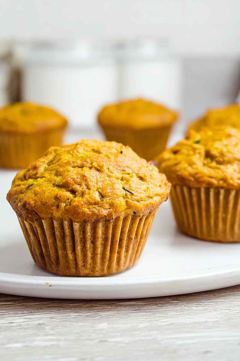 A close-up of golden pumpkin zucchini muffins on a white plate, highlighting their rich texture.
