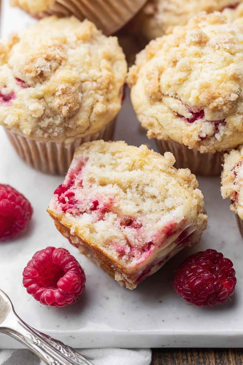Cross-section of a raspberry muffin showing its moist interior dotted with juicy berries, surrounded by fresh raspberries.
