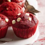 A cluster of red velvet muffins with white chocolate chips, displayed on a white plate with a rustic fork nearby.