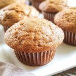 A close-up of golden-brown Sour Cream Applesauce Muffins on a white plate, emphasizing their soft texture and warm, inviting appearance.