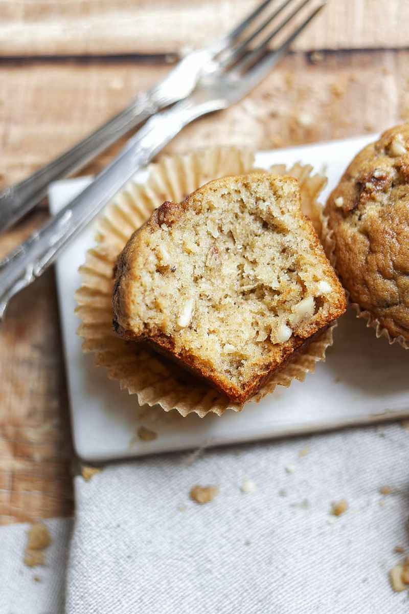 A halved sourdough banana muffin revealing its soft, moist interior, placed on a white plate with crumbs scattered around.