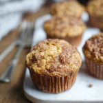 A close-up of golden sourdough banana muffins with a crunchy oat topping, arranged on a white plate.