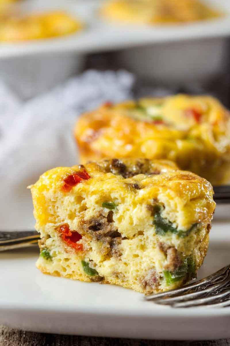 A cross-section view of an egg muffin revealing its creamy interior filled with sausage, bell peppers, and jalapeños.
