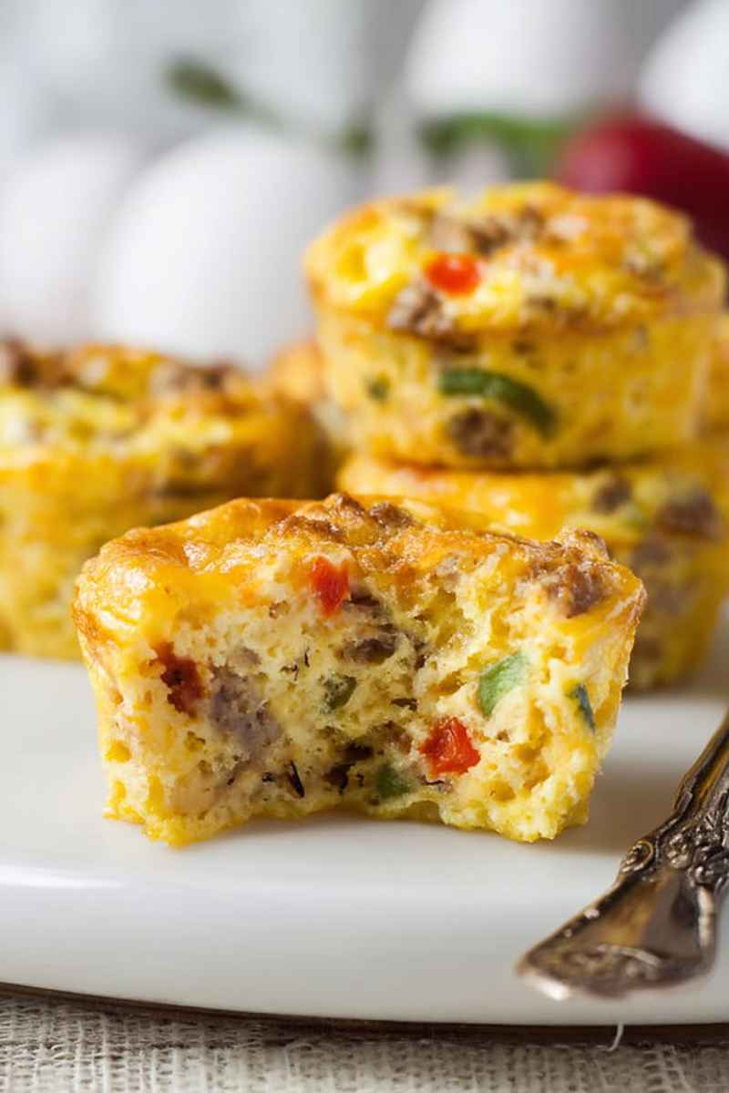 A half-eaten egg muffin showcasing its rich, cheesy interior with chunks of sausage and bell peppers.