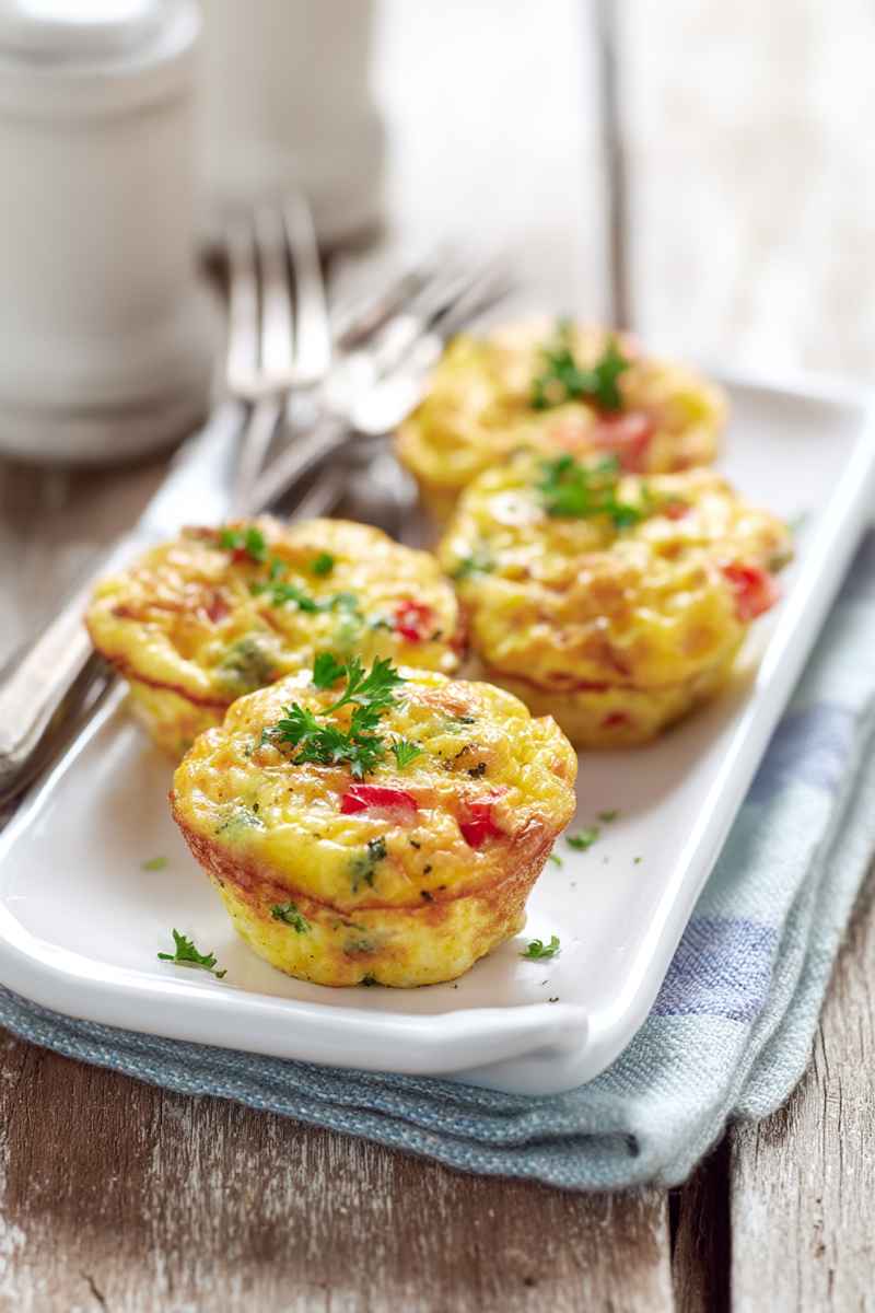 A row of golden egg muffins topped with fresh parsley, served on a white rectangular plate with a blue napkin underneath.