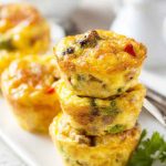 Golden-brown egg muffins stacked on a white plate, filled with colorful bell peppers and sausage, ready to be enjoyed.