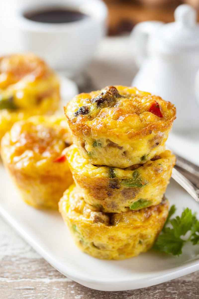 Golden-brown egg muffins stacked on a white plate, filled with colorful bell peppers and sausage, ready to be enjoyed.