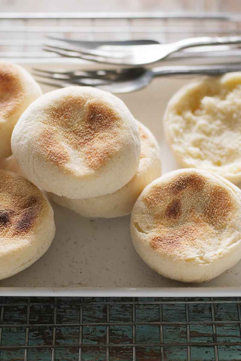 A tray of freshly baked sourdough English muffins with a golden-brown surface and dusted with cornmeal, ready to be enjoyed.
