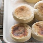 A close-up of golden-brown sourdough English muffins on a white tray, showcasing their inviting texture and color.